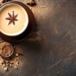 A steaming cup of chai latte with star anise, cinnamon sticks, and other spices